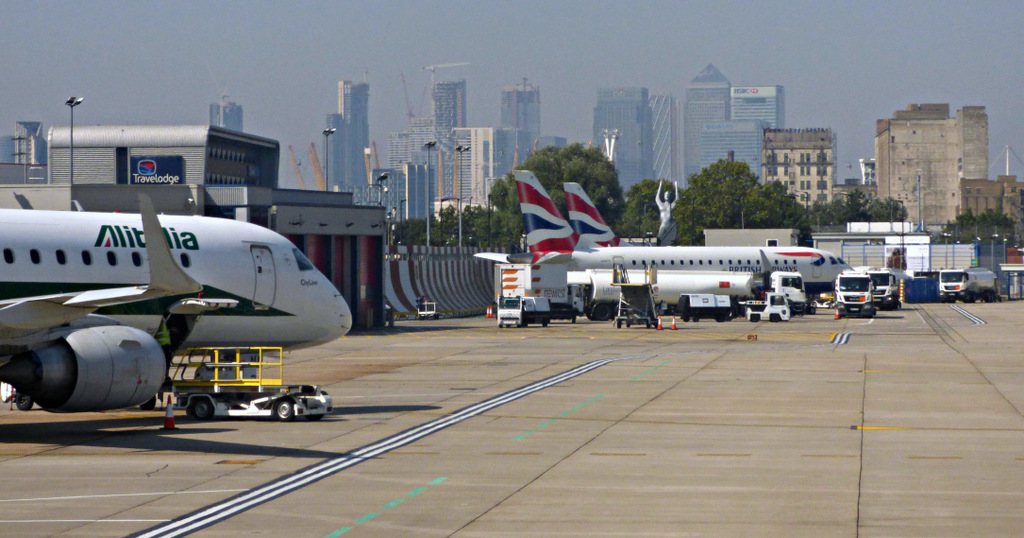Снимка на London City Airport - кацнали самолети на фона на небостъргачите на Канари Уарф