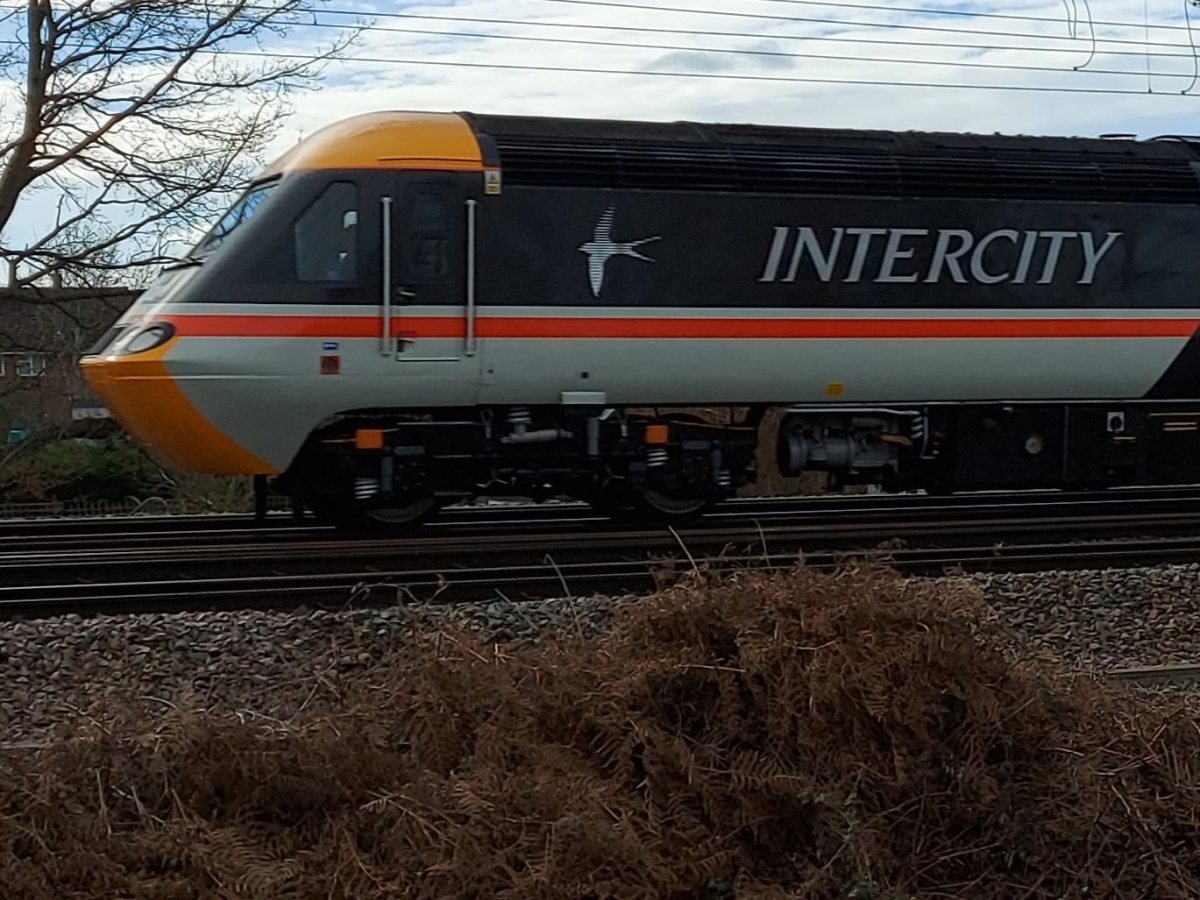 Вертикална фотография в съотношение 4:5, показваща дизеловия локомотив Intercity 125 (номер 43102) в движение по железопътната линия Midland Mainline в Англия. В долната част на изображението, върху леко затъмнен градиент, е поставено информационно заглав
